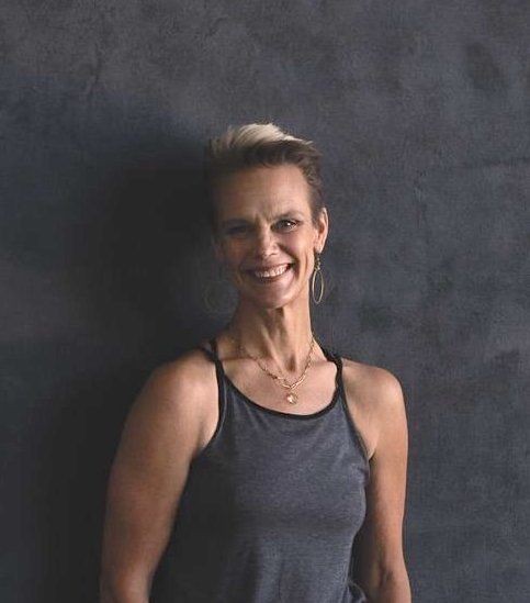 Smiling woman in a dark tank top standing against a textured gray wall.
